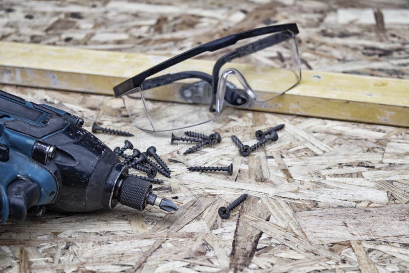 Power drill with goggles for eye safety and building level against the background of OSB panel. Concept on the topic of. Construction and repair royalty free stock photo